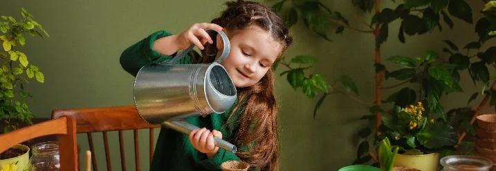 Kind gießt Pflanze mit Gießkanne